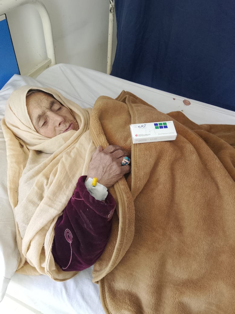 An elderly patient resting in a hospital bed with her medicine